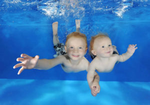 Swimming lessons - two young boys swimming underwater holding hands